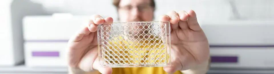 A person that holds a microplate in his hands.